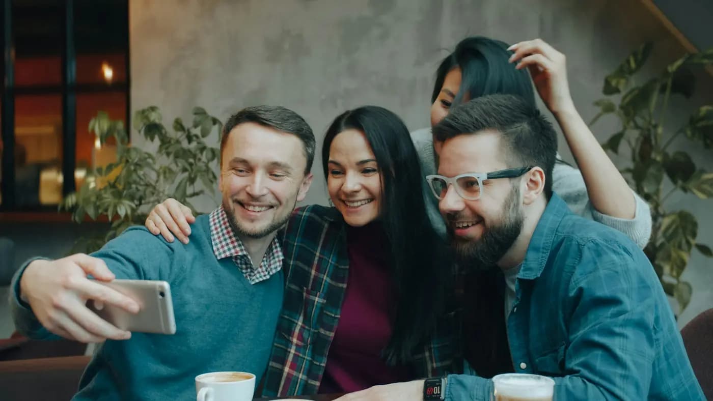 Drie vrienden lachen samen naar een telefoon in een café