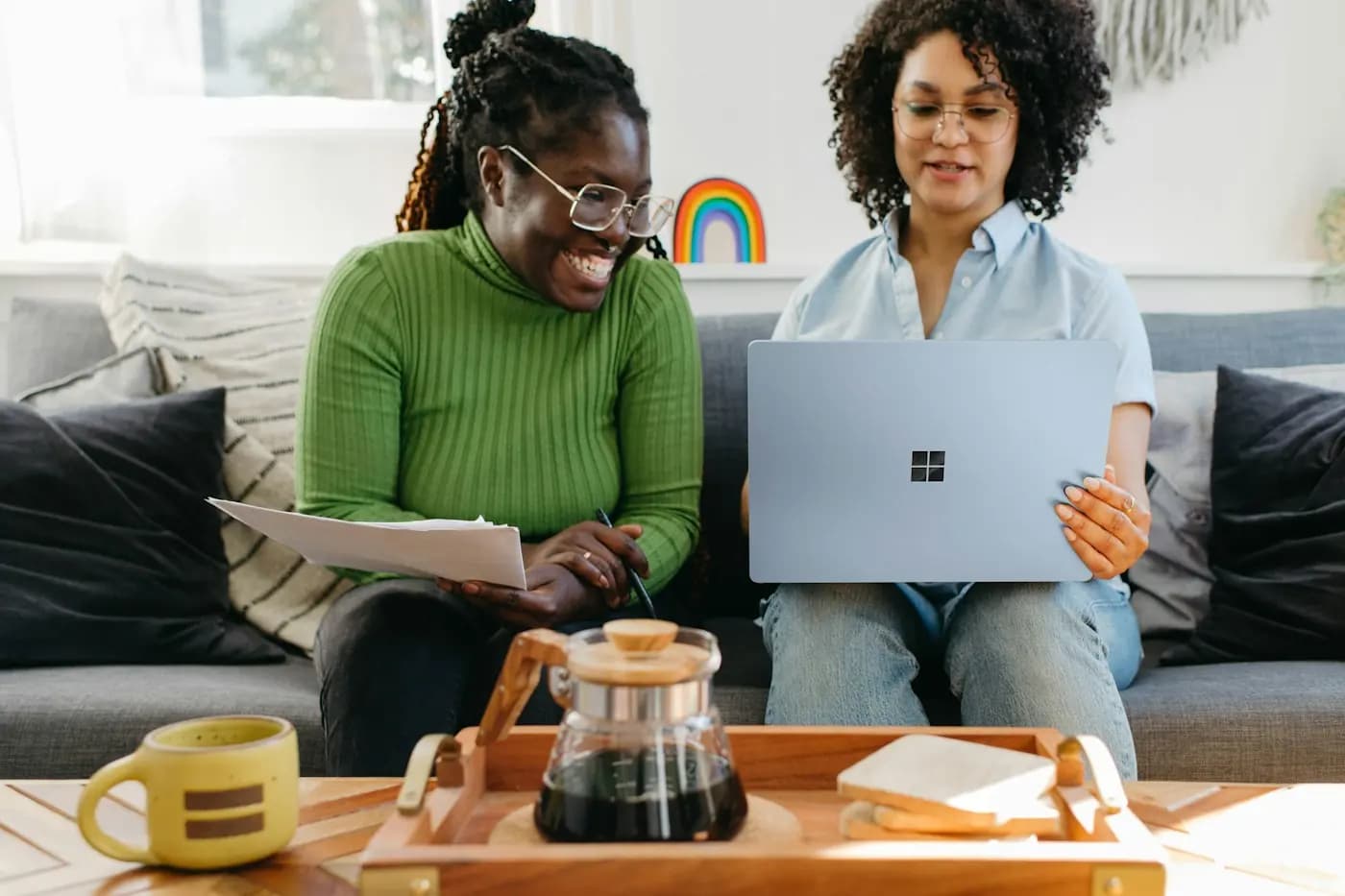 Twee vrouwen werken lachend samen op de bank met een laptop